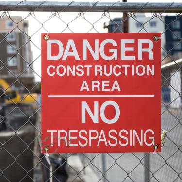 A red sign that says 'Danger Construction Area No Trespassing' in white lettering. The sign is attached to a chain link fence.