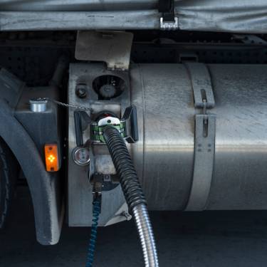 The fuel tank on an industrial truck receives fuel through a supply hose. A yellow light sits by the front wheel.