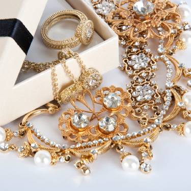 An assortment of gold jewelry with diamonds and pearls on a white background. There are necklaces, brooches, and rings.