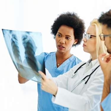 A team of medical professionals reviews an x-ray of a patient’s lungs and discusses their preferred diagnosis.