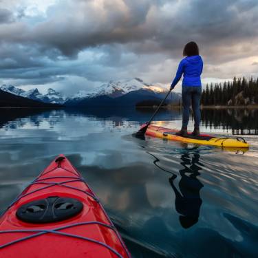 A woman paddleboarding across a Canadian lake. There is also a kayaker behind her and the water is calm.