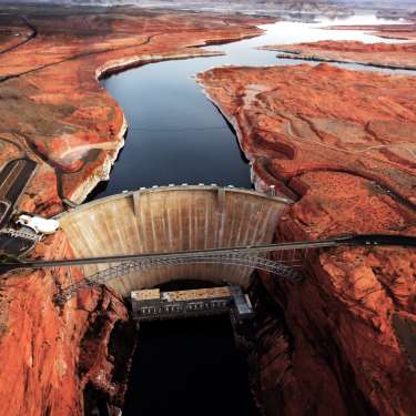 An aerial view shows the Glen Canyon dam on the Colorado River. Around it is the red ground of the canyon.