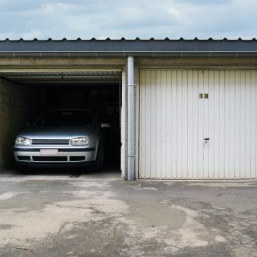 A classic car parked in a multi-unit garage. The garage door is open and the car is backed into the parking spot.