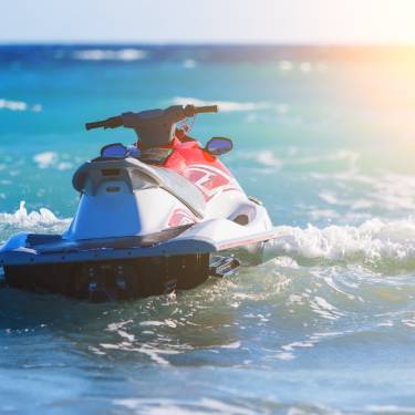 A jet ski is floating on a wave in the ocean with other waves and a sunset shines through the background.